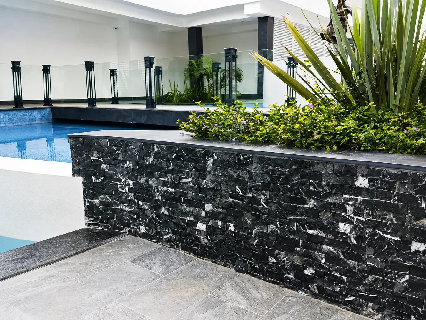 Finished black stone pool wall paired with light grey exterior paving